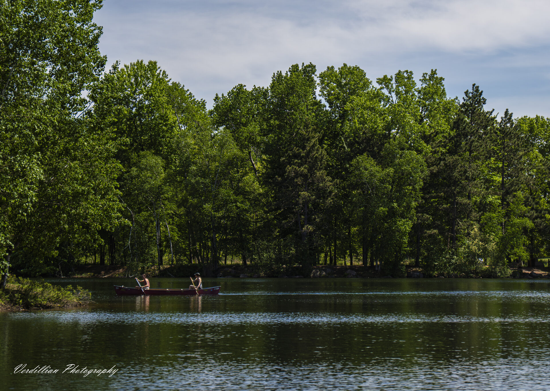 Two people canoeing on a calm, tree-lined lake